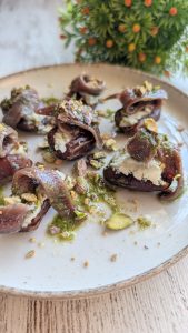 Dátiles carnosos abiertos y rellenos de queso azul y anchoa, regados con salsa pesto y espolvoreados con pistachos picados.