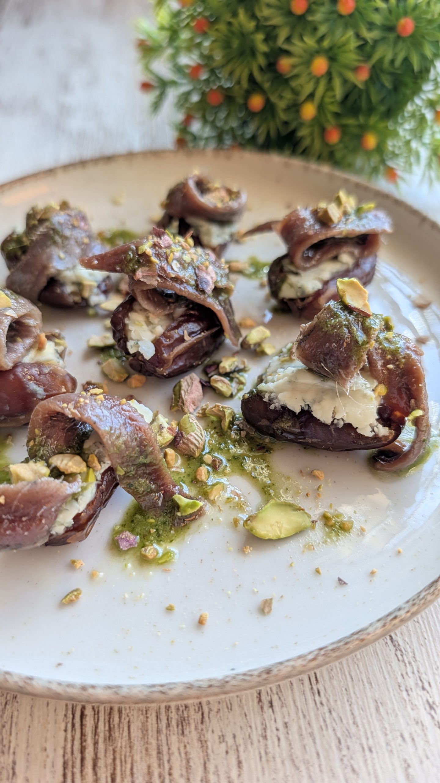 Dátiles carnosos abiertos y rellenos de queso azul y anchoa, regados con salsa pesto y espolvoreados con pistachos picados.