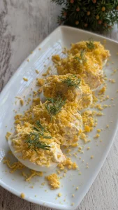 Mitades de huevos rellenos de crema de salmón ahumado y queso, espolvoreados con yema rallada y eneldo fresco en una fuente.
