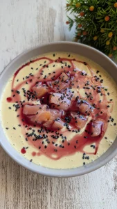 Plato hondo con mazamorra de mango de color amarillo cremoso, decorada con tiras de salmón ahumado, semillas de sésamo y un hilo de aceite de oliva rojo.