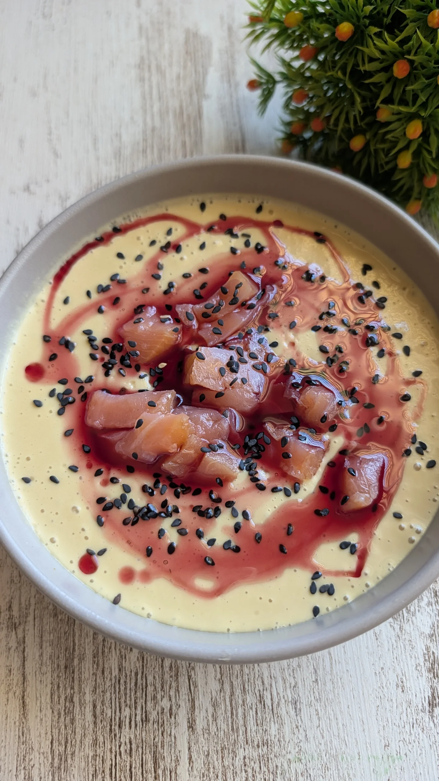 Plato hondo con mazamorra de mango de color amarillo cremoso, decorada con tiras de salmón ahumado, semillas de sésamo y un hilo de aceite de oliva rojo.