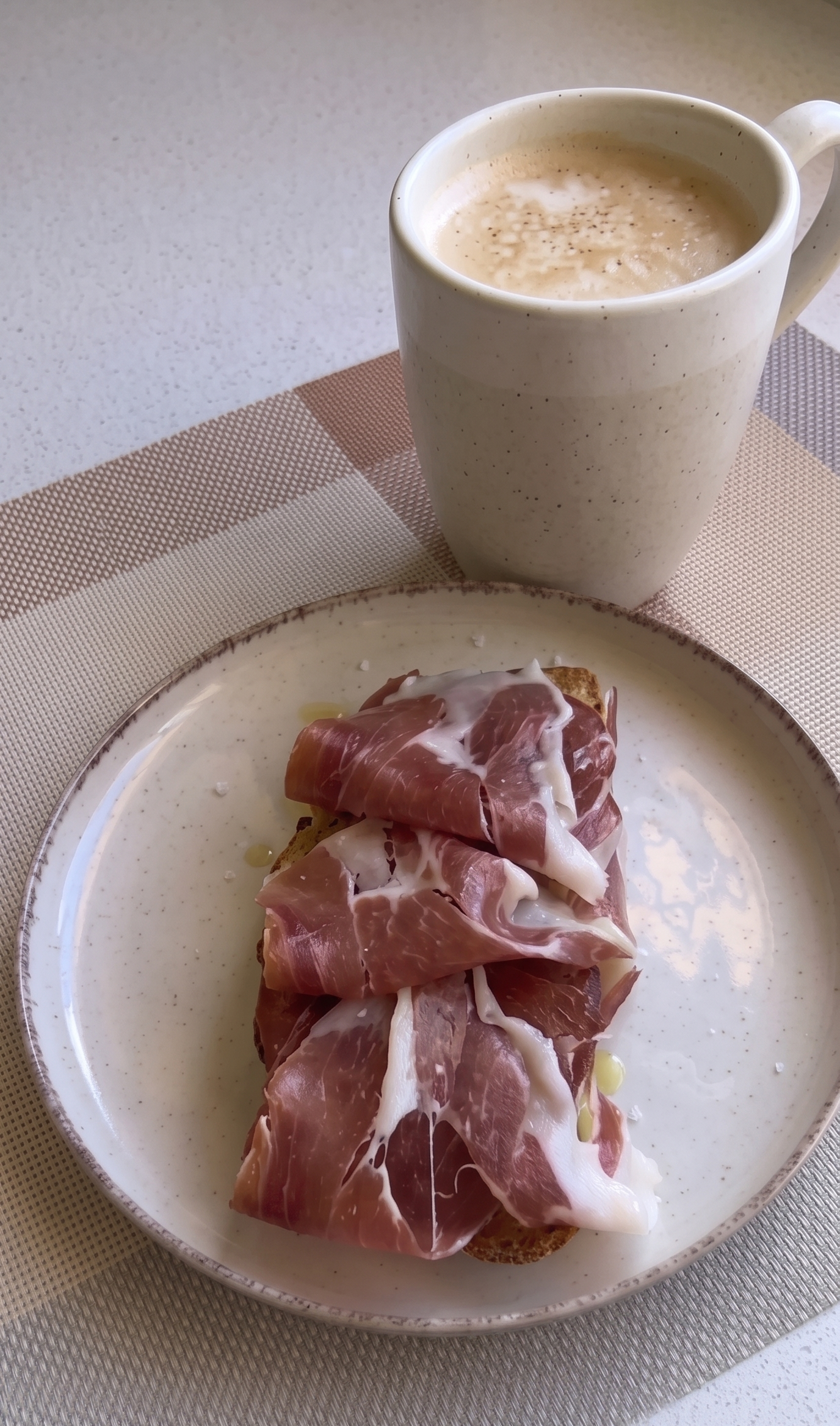 Rebanada de pan artesanal tostado regada con aceite de oliva virgen extra, cubierta con rodajas de tomate fresco y lonchas de jamón ibérico.