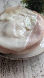Mollete abierto tostado con tomate fresco, jamón cocido y lonchas de queso de cabra derretido por encima.