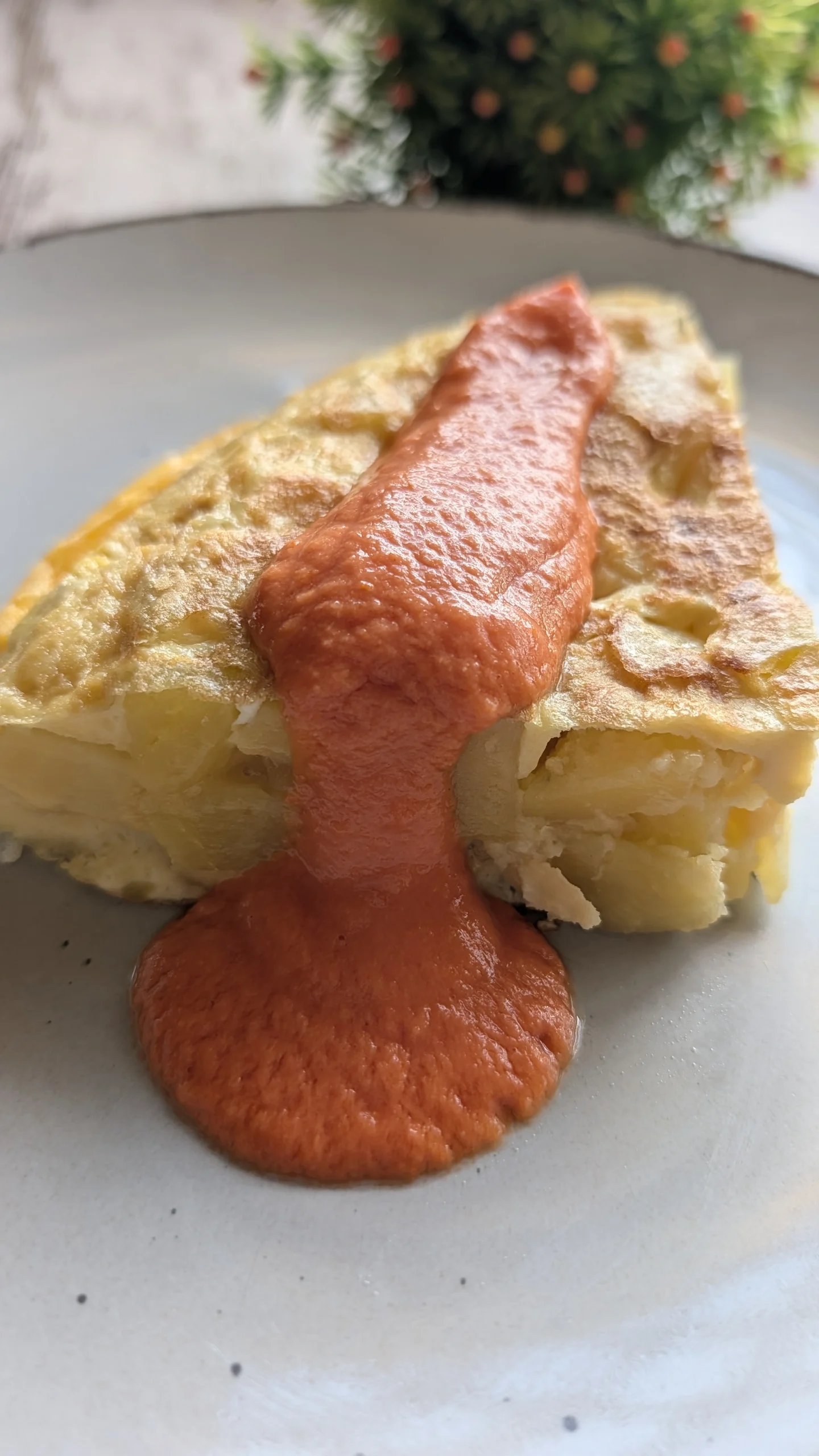 Porción de tortilla de patatas casera jugosa servida en un plato acompañada de una cata de salmorejo tradicional.
